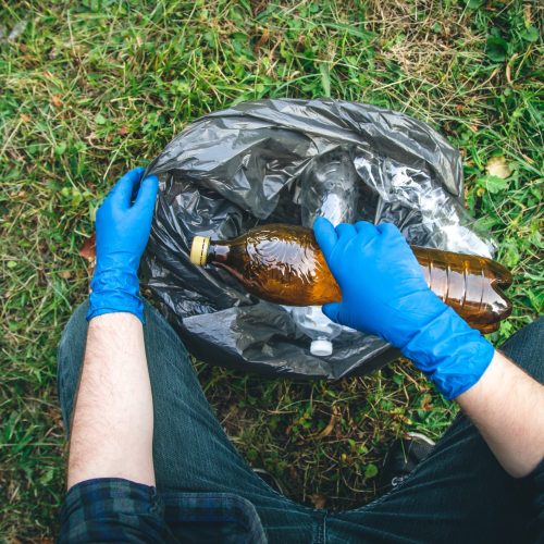 A man puts a plastic bottle in a garbage bag, the concept of forest cleaning and love for nature.