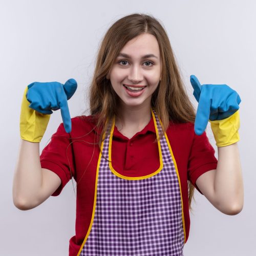 young beautiful girl in apron and rubber gloves  smiling pointing with fingers down standing over white background